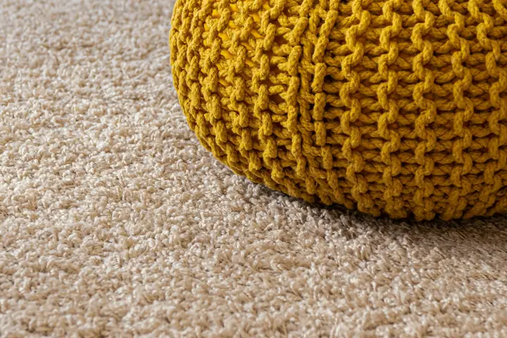 Clean beige carpet with a yellow knitted pouf